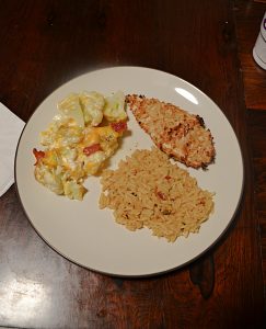 A plate topped with a crispy almond coated chicken breast, a pile of rice, and loaded cauliflower