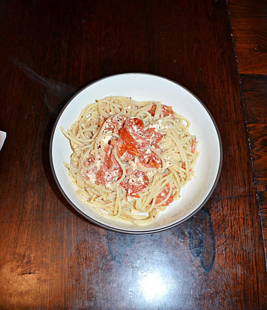 A bowl of spaghetti mixed with pieces of cherry tomatoes and feta in it. 