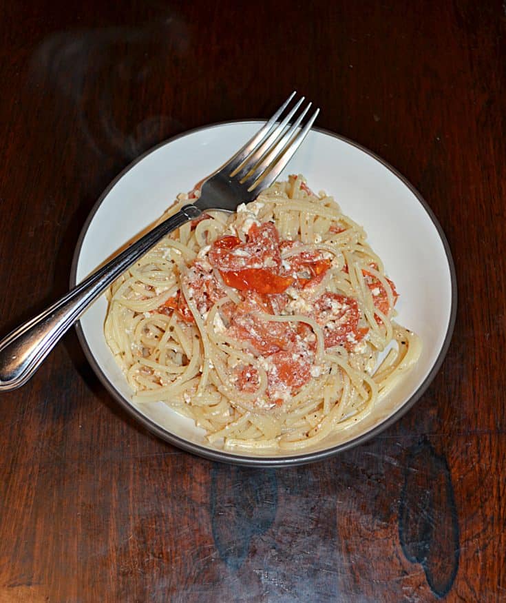 A bowl of spaghetti combined with tomatoes and feta with a fork sitting on top of the bowl.