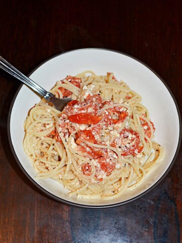 A bowl of spaghetti combined with tomatoes and feta with a fork sticking out of it.