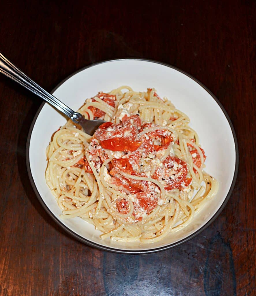 A bowl of spaghetti combined with tomatoes and feta with a fork sticking out of it. 