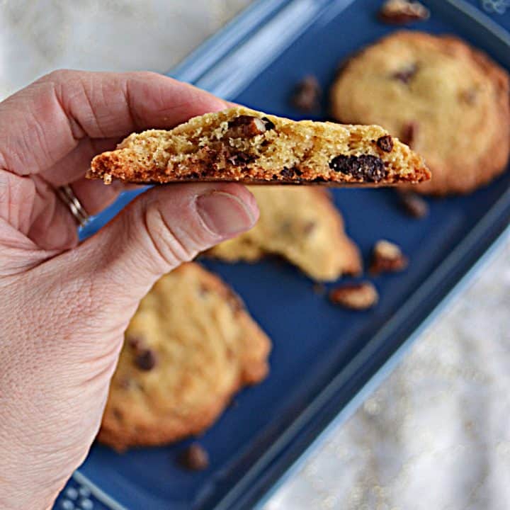 A close up view of a caramel turtle cookie with a bite out of it and a platter of cookies in the background.