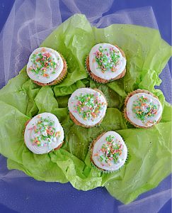Six carrot cake cupcakes topped with cream cheese frosting and sprinkles on a green background.