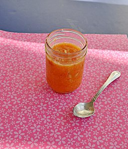 A jar of bright orange Kumquat Jam with a spoon next to it.