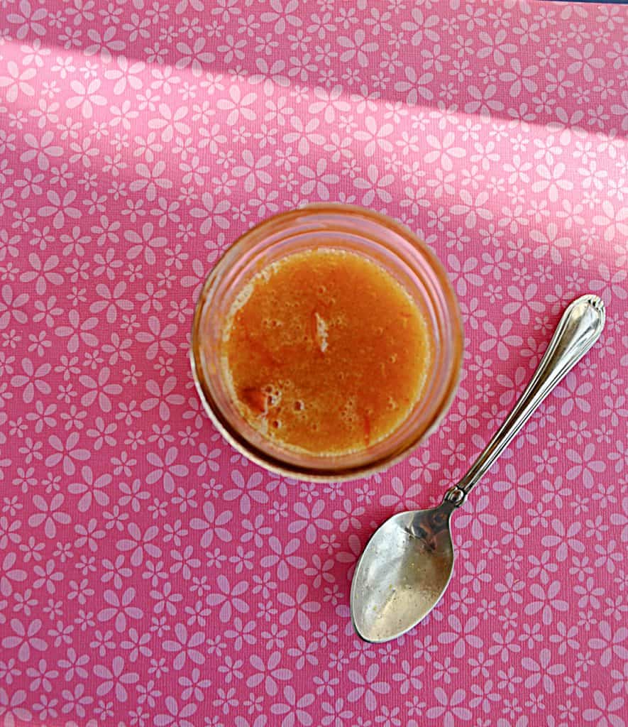 An overhead view of a jar of Kumquat Jam with a spoon next to it. 