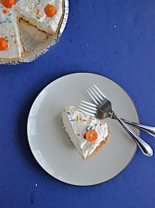 A top view of a slice of No Bake Kumquat Pie with a kumquat on top and two forks on the plate and the pie with a slice cut out of it in the upper left hand corner.