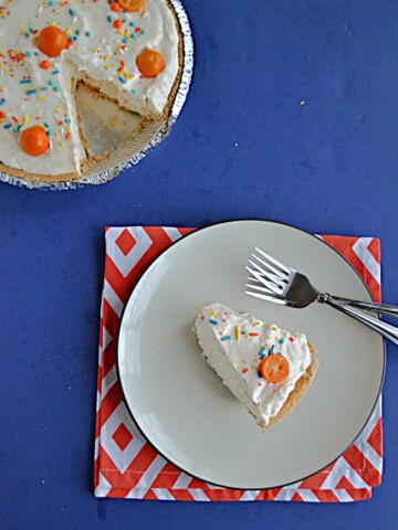 A slice of No Bake Kumquat Pie with a kumquat on top and the pie with a slice cut out of it in the upper left hand corner.