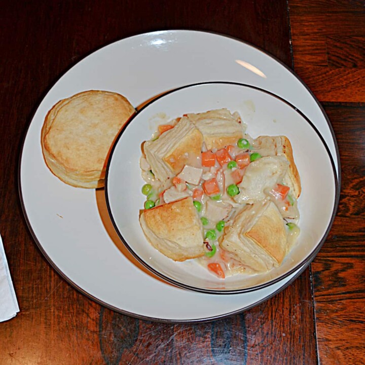A bowl filled with chicken pot pie topped with biscuits with a biscuit on the side.