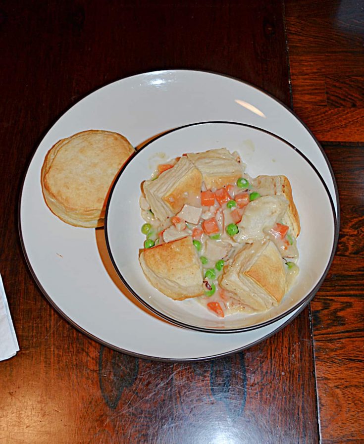 A bowl filled with chicken pot pie topped with biscuits with a biscuit on the side.