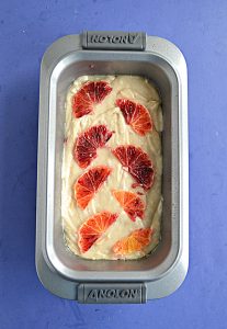 A loaf pan with blood orange cake batter and blood orange slices on top.