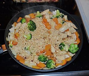 A skillet filled with ramen noodles, fresh vegetables, and chicken.