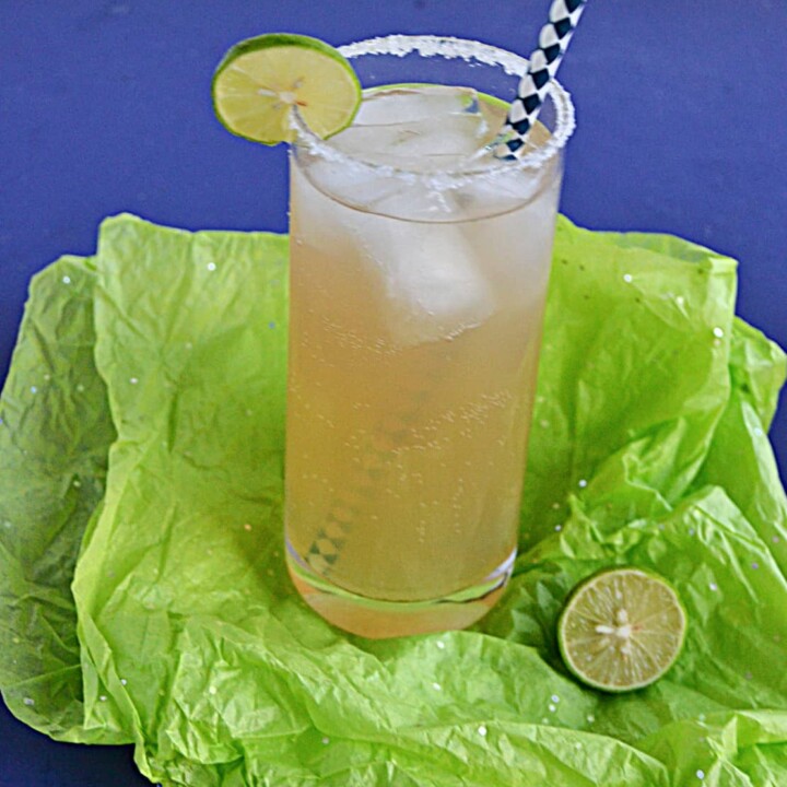 A glass of key lime margarita on the rocks with a lime wedge and salt on the rim and a straw in the glass.