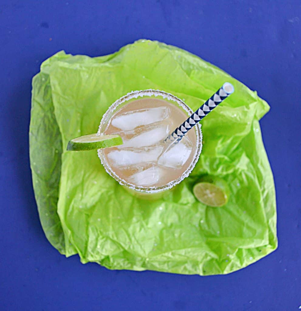 An overhead view of a glass of key lime margaritas with ice in the glass, a lime wedge on the rim, and a straw in the glass. 
