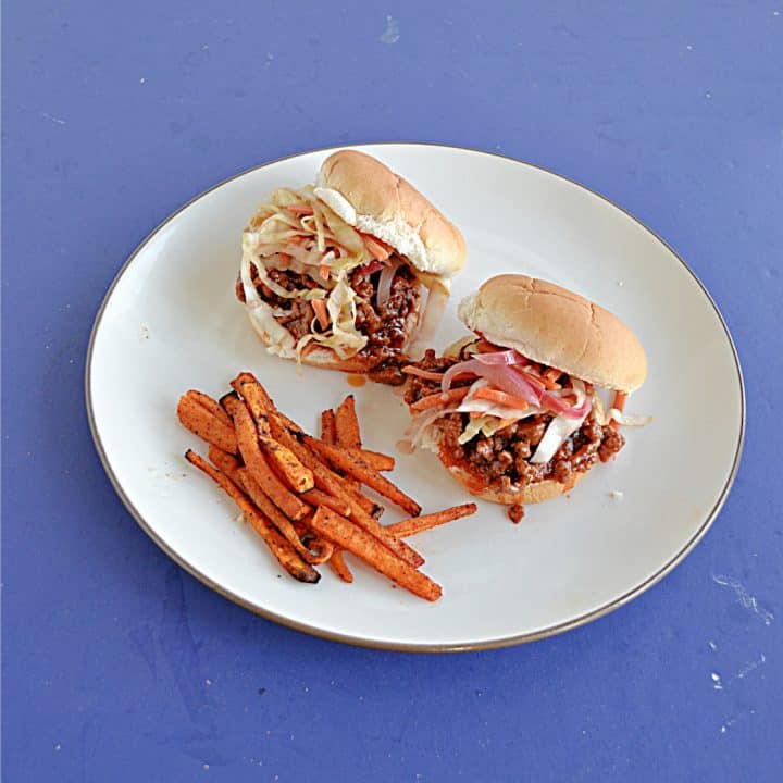 Two Korean BBQ Sloppy Joe Sandwiches topped with pickled vegetables and a side of sweet potato fries.