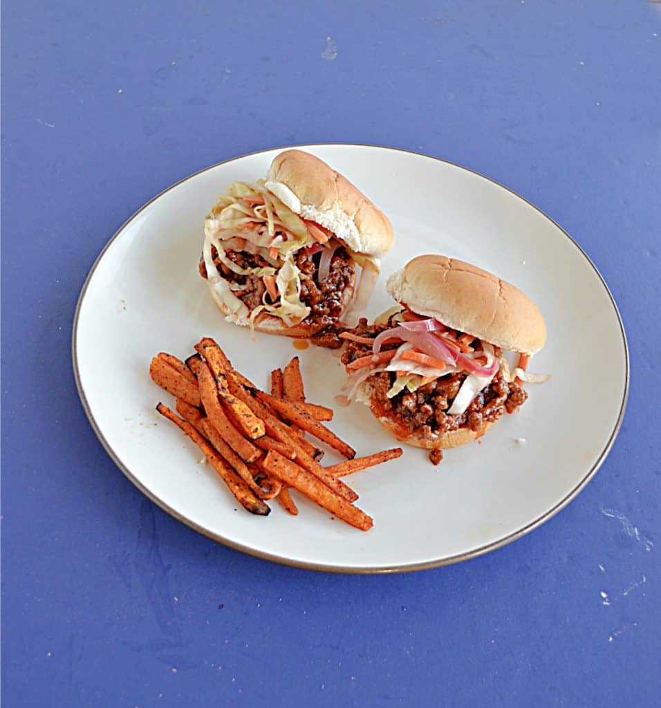 Two Korean BBQ Sloppy Joe Sandwiches topped with pickled vegetables and a side of sweet potato fries. 