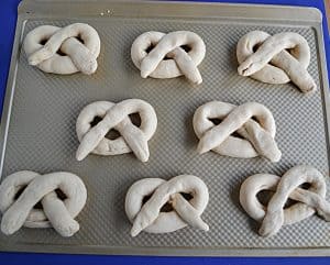 A baking sheet with 8 unbaked sourdough soft pretzels on it.