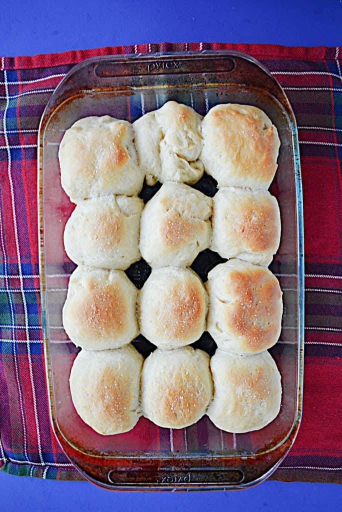 A glass baking dish with a dozen golden brown rolls in it.