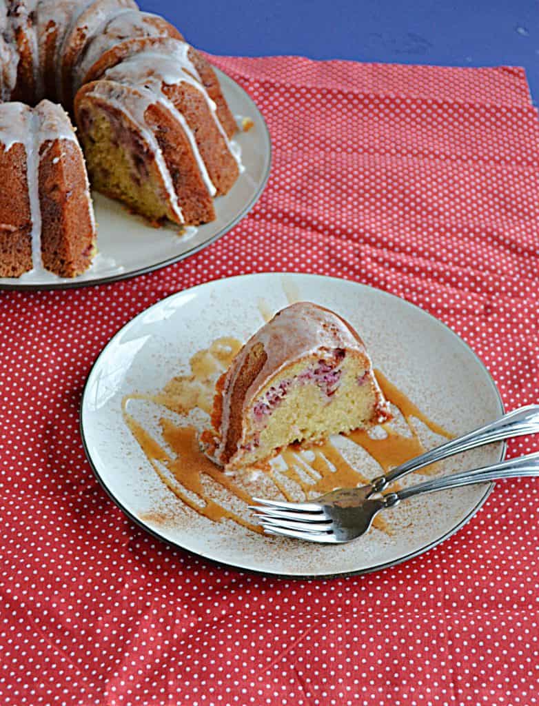 A slice of strawberry Bundt cake on a plate drizzled with caramel and two forks with the cut Bundt cake behind it. 