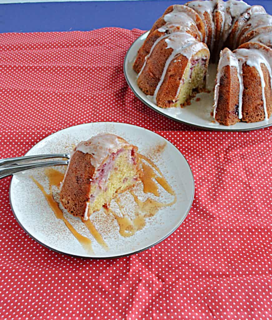 A slice of strawberry Bundt cake on a plate drizzled with caramel and two forks with the Bundt cake behind it.