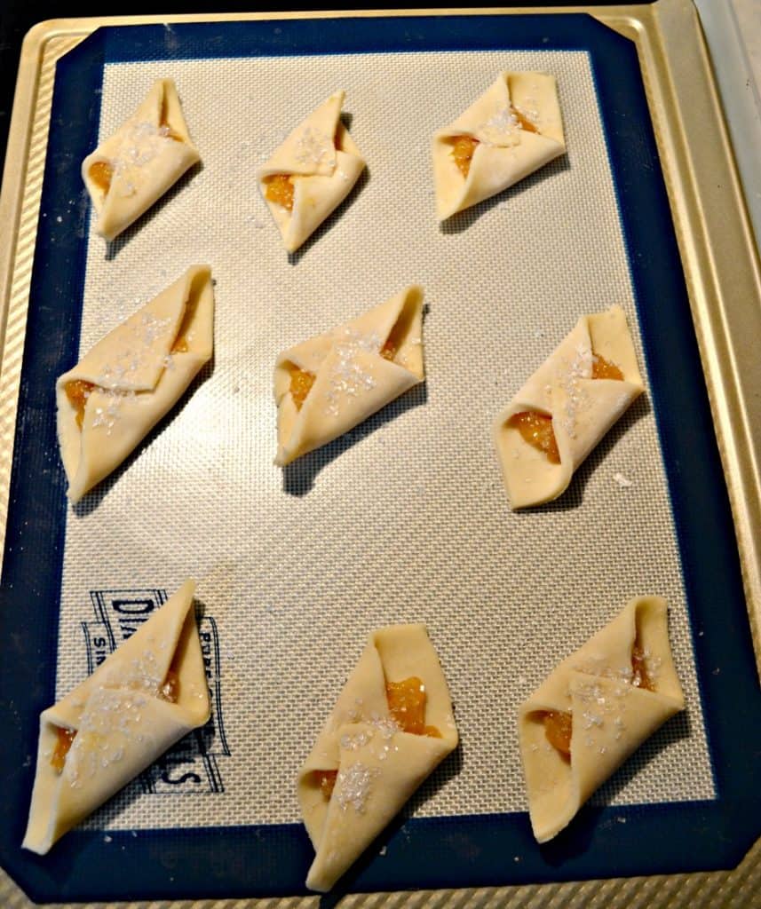 A cookie sheet topped with 9 folded Polish Cream Cheese cookies filled with apricot jam.