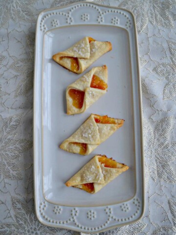 A platter with four Polish Cream Cheese Cookies filled with apricot jam.