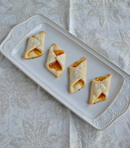 A white platter with four Polish Cream Cheese Cookies filled with apricot jam.
