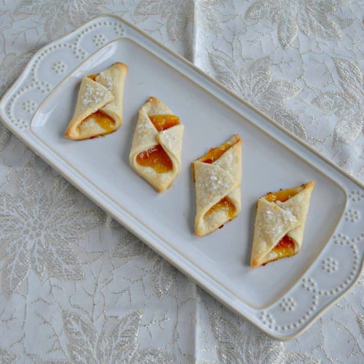 A white platter with four Polish Cream Cheese Cookies filled with apricot jam.