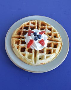 A plate with a Belgium waffle topped with whipped cream, blueberries, and strawberries.