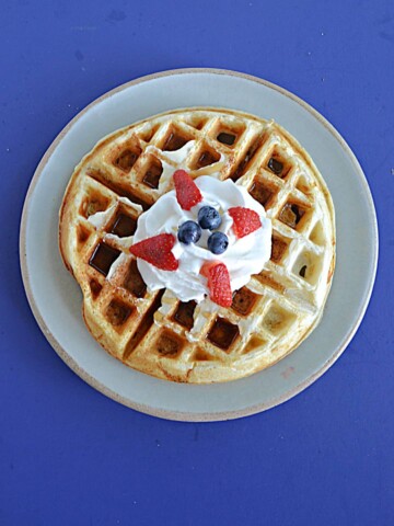 A top view of a Belgium Waffle topped with whipped cream and berries.