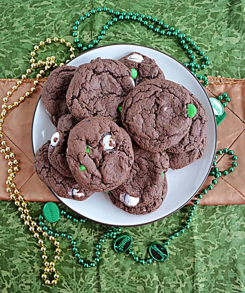 A plate piled high with chocolate cake mix cookies surrounded by green and gold beaded necklaces. 