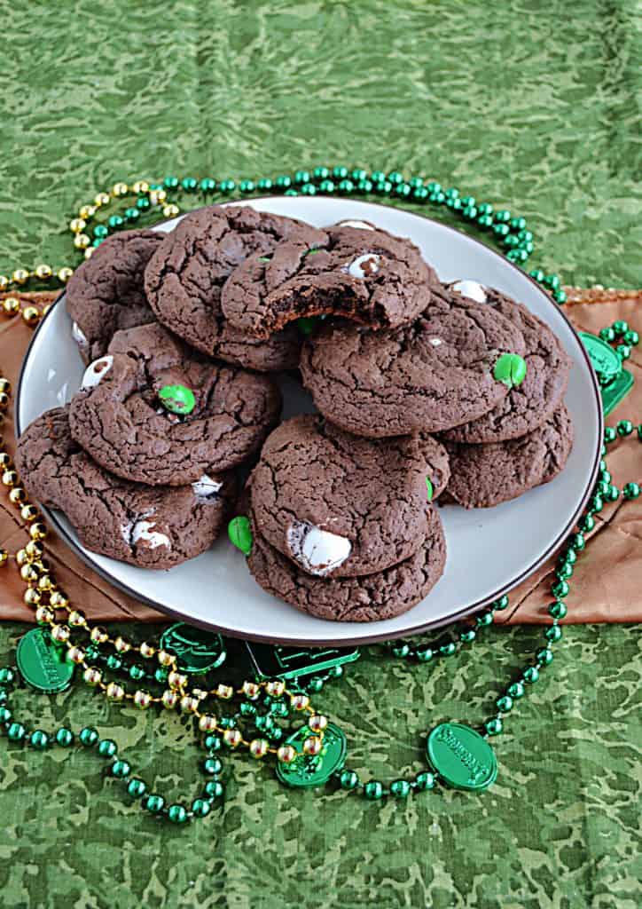 A front view of a plate piled high with chocolate cake mix cookies surrounded by green and gold beaded necklaces. 