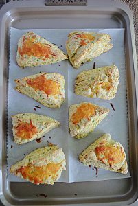 A baking sheet with 8 scones on it topped with cheese.
