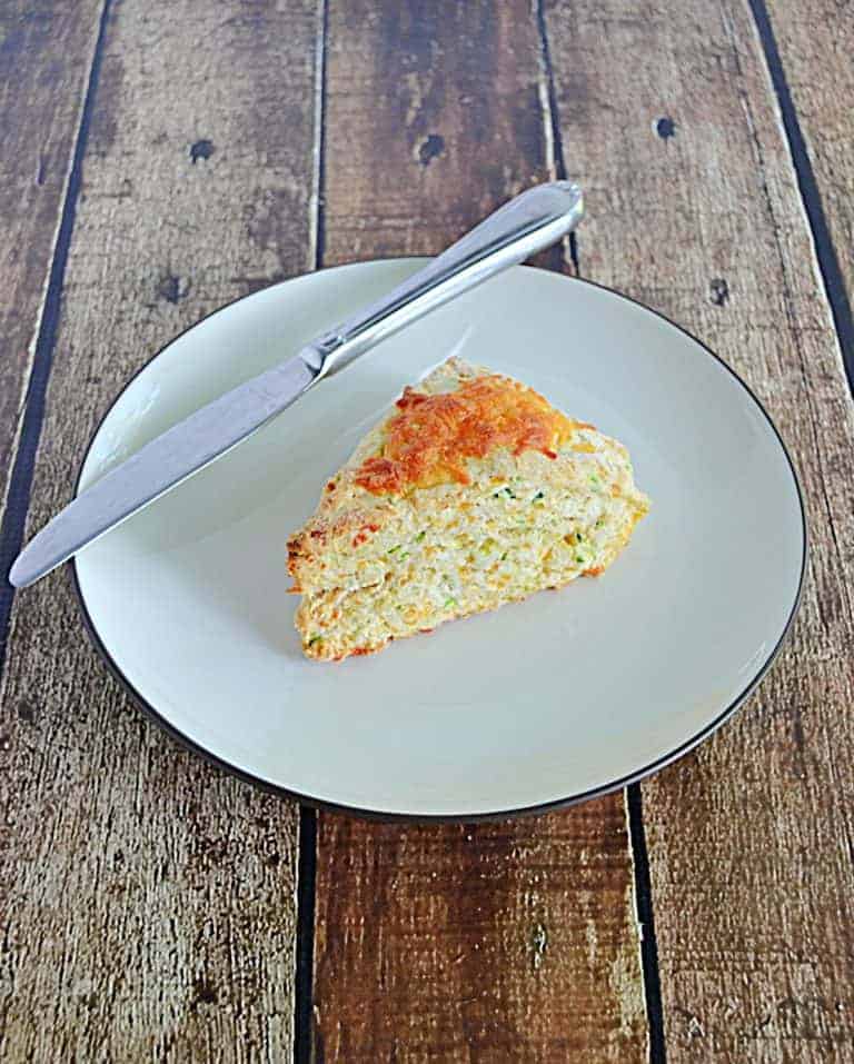A plate with a giant Zucchini Cheddar scones with a knife on the plate.