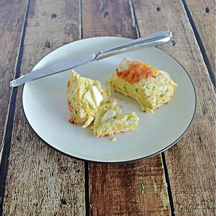 A plate with a zucchini cheddar scones cut in half and smeared with butter and a knife on the plate.