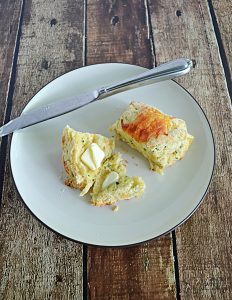 A plate with a zucchini cheddar scones cut in half and smeared with butter and a knife on the plate.
