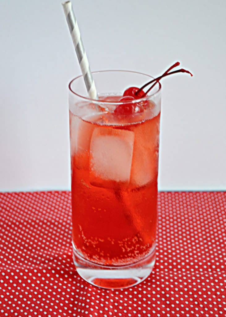 A tall glass filled with Cherry Vanilla Bourbon Fizz with two cherries on top and a straw in the glass.