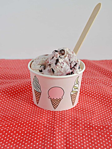 A bowl filled with No Churn Chocolate Cherry Ice Cream with a wooden spoon sticking out of it.