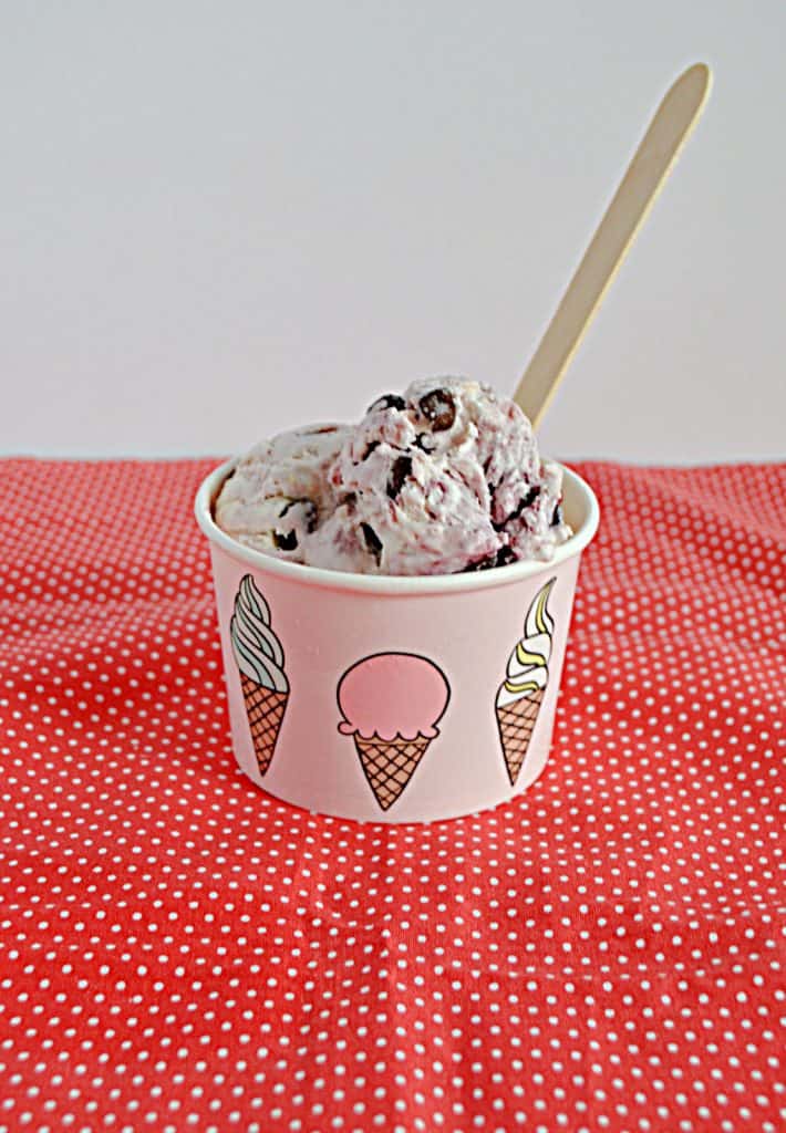A bowl filled with No Churn Chocolate Cherry Ice Cream with a wooden spoon sticking out of it. 
