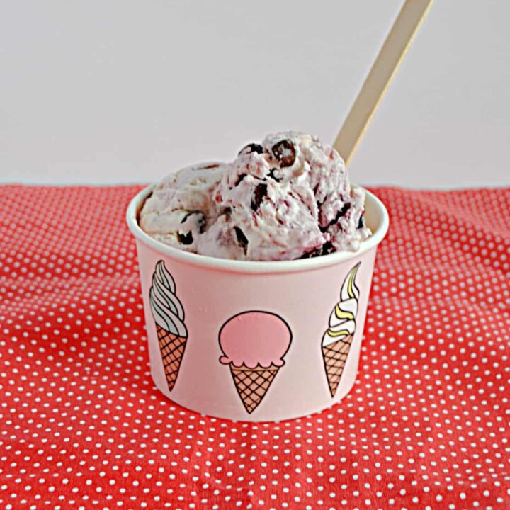 A bowl filled with No Churn Chocolate Cherry Ice Cream with a wooden spoon sticking out of it.