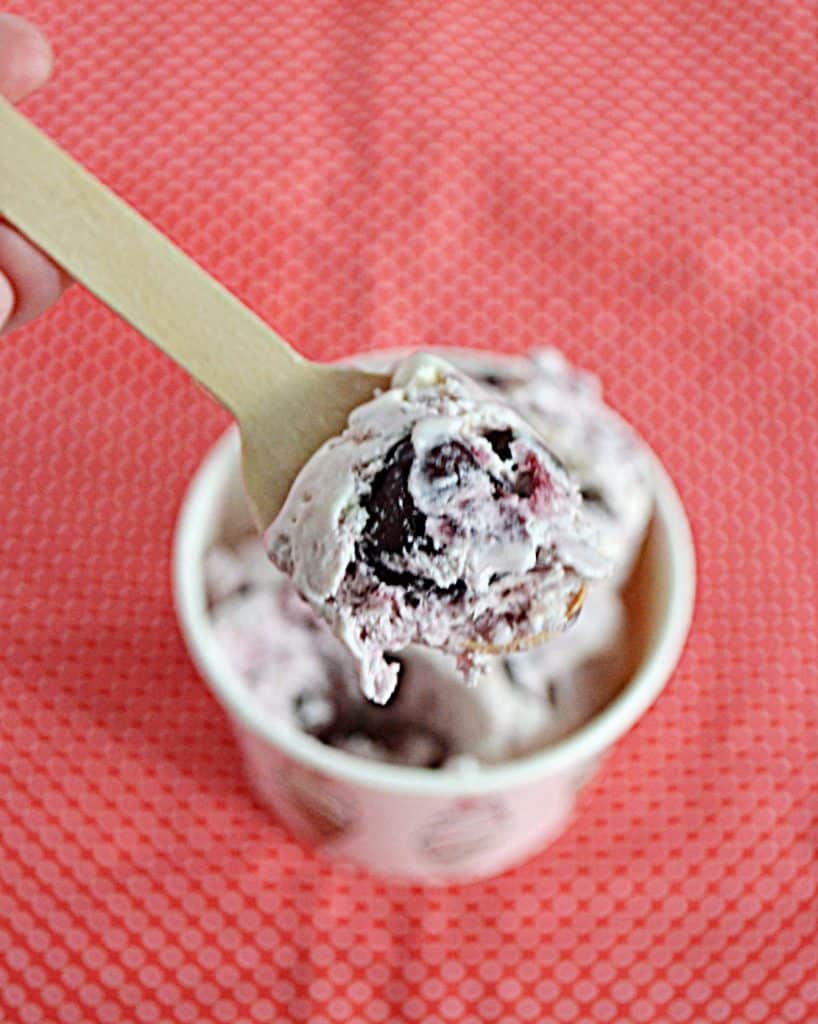 Close up view of a spoonful of Chocolate Cherry Ice Cream on a wooden spoon with a bowl of ice cream in the background.
