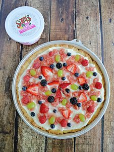 Top view of A fruit pizza topped with watermelon salsa and fresh fruit with a container of watermelon salsa behind it.