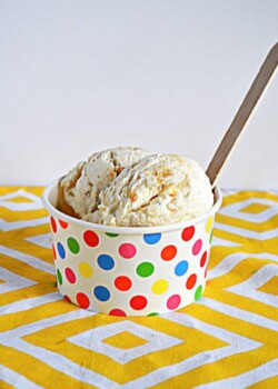 A rainbow dotted bowl with two scoops of Lemon Shortbread Ice Cream and a wooden spoon in it.