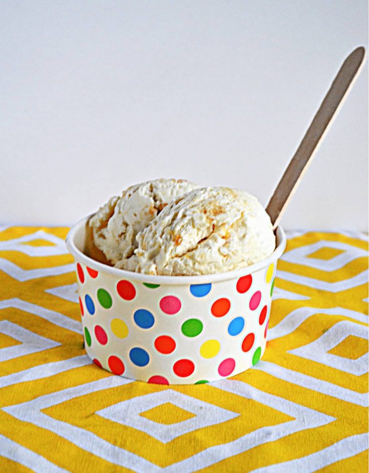 A rainbow dotted bowl with two scoops of Lemon Shortbread Ice Cream and a wooden spoon in it.