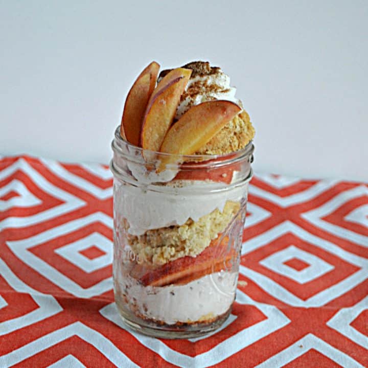 A jar layered with cinnamon whipped cream, fresh peaches, and sweet biscuits with peaches on top.