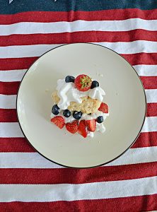 A plate with a shortcake made with sweet biscuits, whipped cream, strawberries, and blueberries.