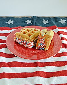 A plate with two waffle ice cream sandwiches rolled in red, white, and blue sprinkles.