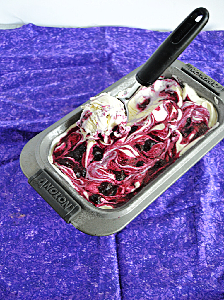 A pan of blueberry swirl ice cream with an ice cream scoop in the ice cream.