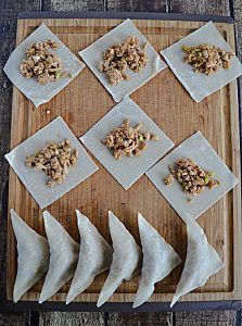 A cutting board with 6 stuffed chicken gyoza and six Chicken Gyoza that are laying on the wonton wrapper wready to be wrapped.