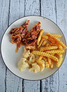 A plate piled with crinkle cut fries, ranch cauliflower, and barbecue chicken tenders topped with bacon onion jam.