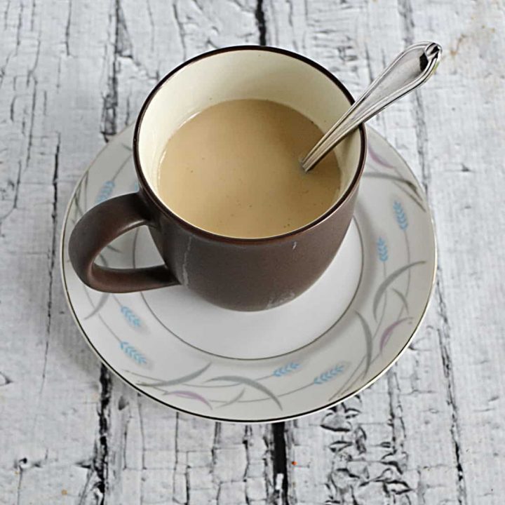 A cup of milk tea on a saucer with a spoon in the cup.